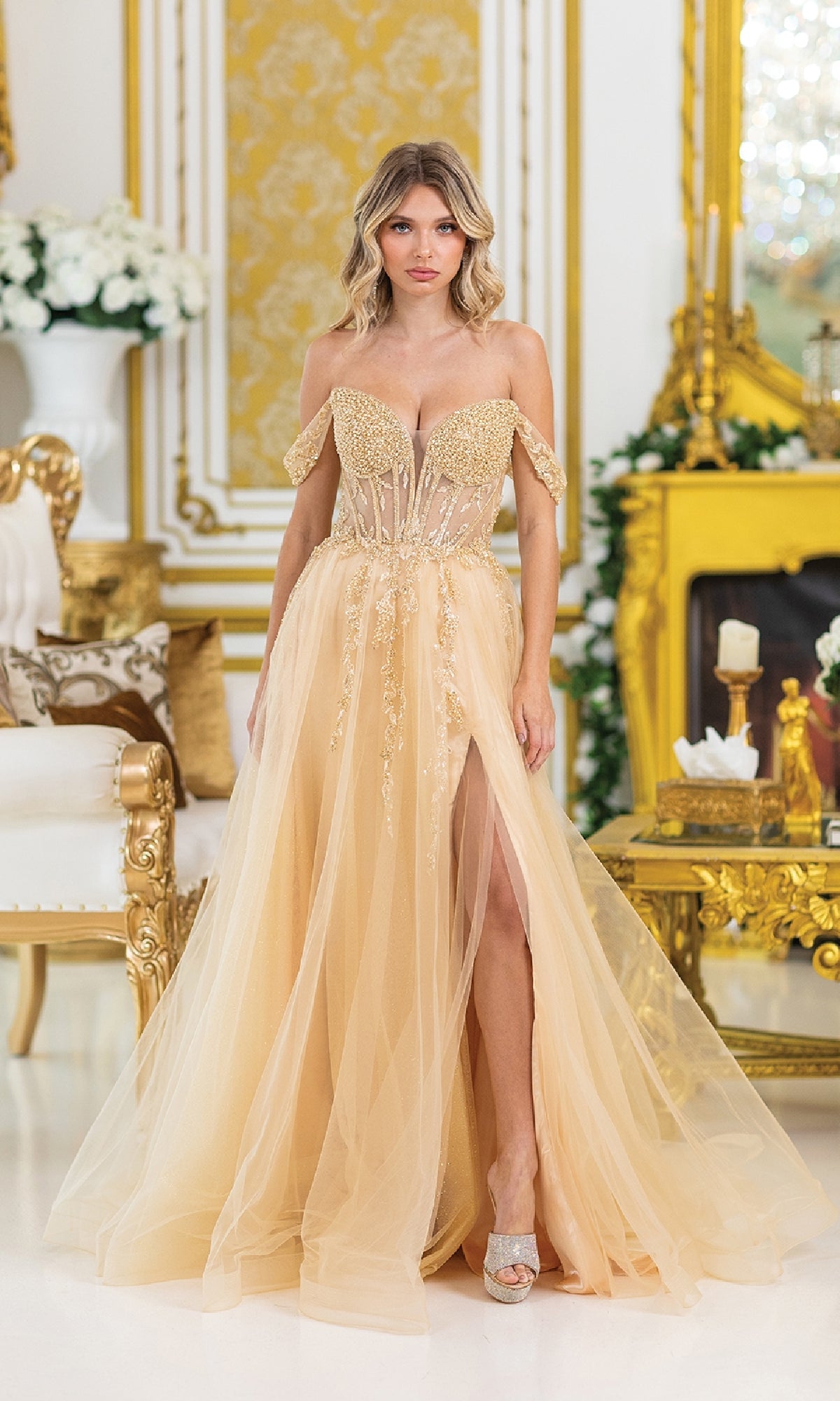 A woman wearing the Lace-Up Long A-Line Prom Dress: Dancing Queen 4490 stands in a luxurious room with ornate gold decor and white floral arrangements.